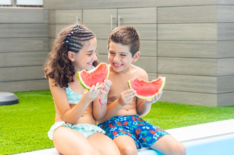 Hermano y hermana comiendo sandía junto a la piscina 