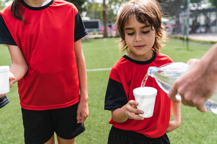 Two children drinking water as a form of recovery during a soccer match.