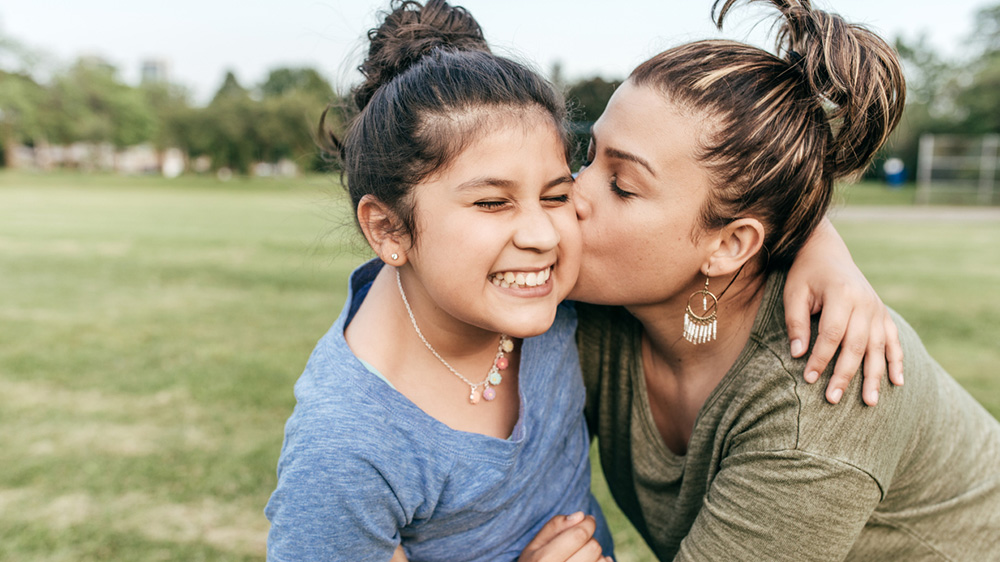 smiling girl being kissed on the cheek by her mother.