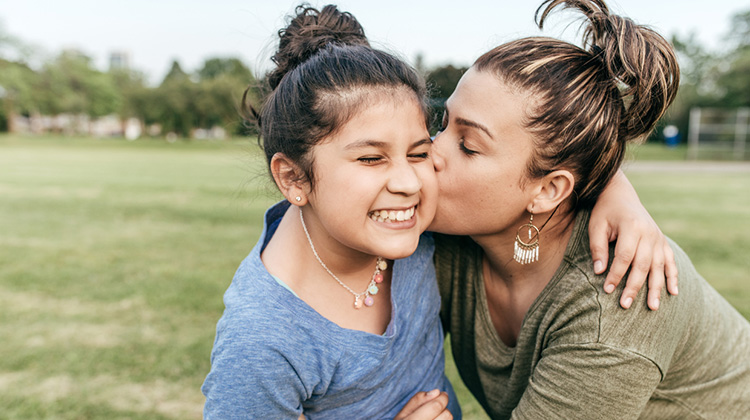 smiling girl being kissed on the cheek by her mother.