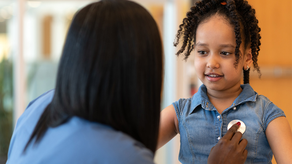 enfermera examina el corazón de una niña afro americana.