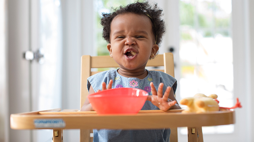 toddler girl eating on a high chair.