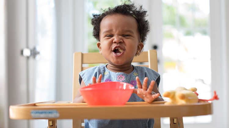 toddler girl eating on a high chair.