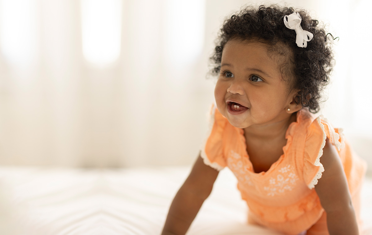 dark skinned baby girl wearing a frilly orange shirt.