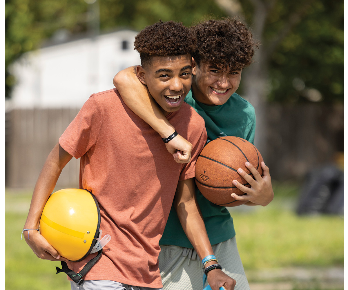 two teenage boys smiling as they do sports outside.