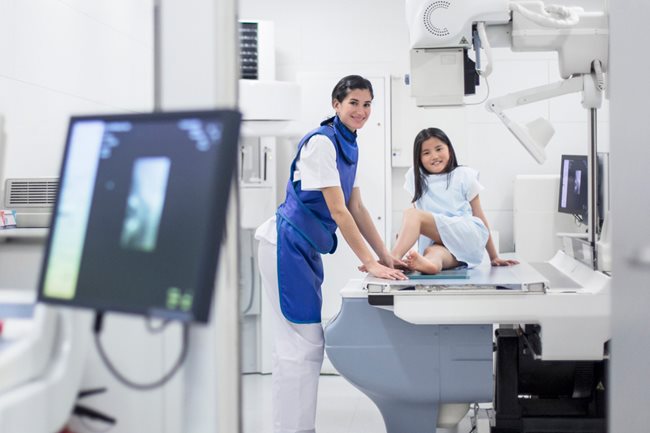 técnico de rayos equis y niña sentada en la mesa de exámen.